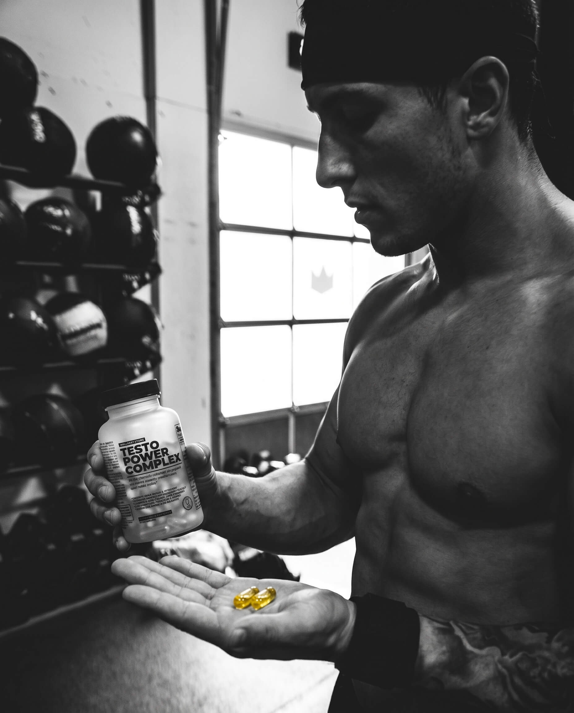 Black and white portrait — a man examines two yellow capsules of Testo Power Complex in his hand
